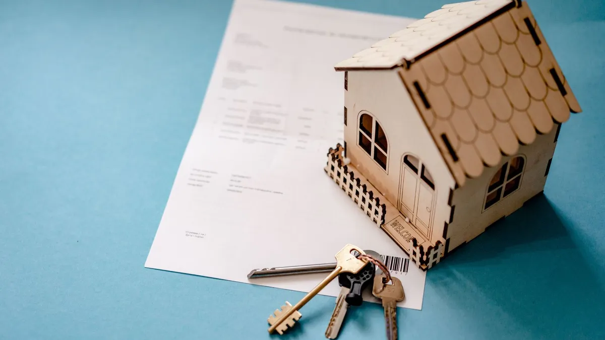 House keys resting on a mortgage contract next to a small wooden model house